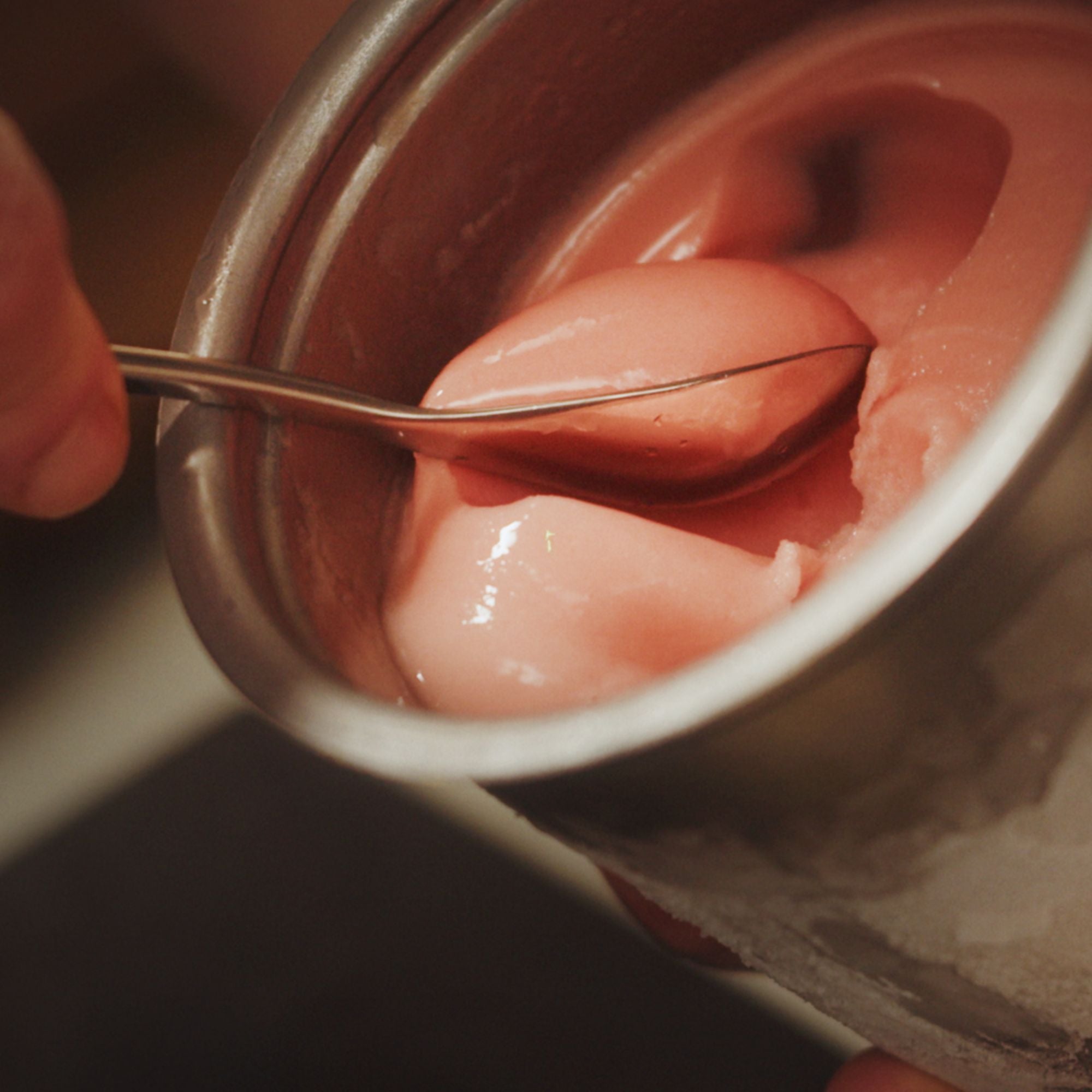 Pink ice cream being scooped from a container with a rocher spoon.